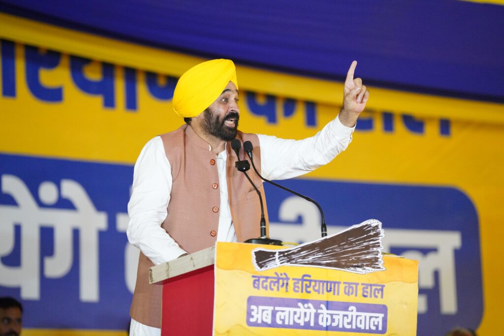 a man standing at a podium with a microphone and a yellow turban